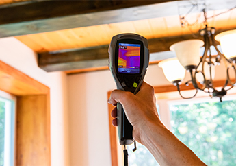 A contractor using a heat sensor where the wall and ceiling meet inside a home.